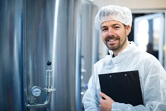 Technician in protective clothing holding a clipboard in a processing area