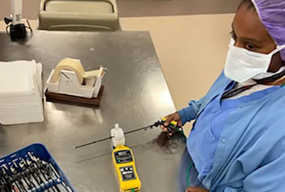 Sterile processing technician in scrubs inspecting a surgical instrument