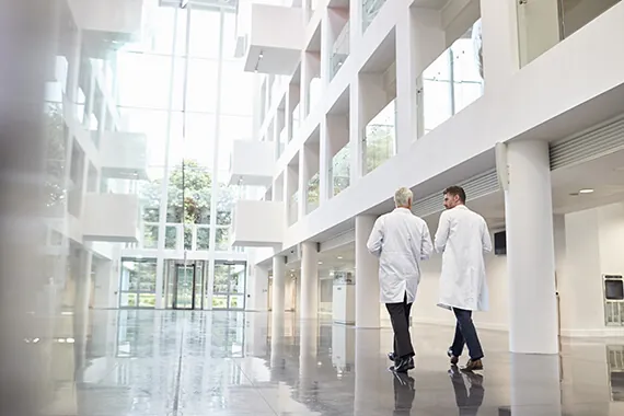 Two physicians walking through a bright, modern hospital atrium